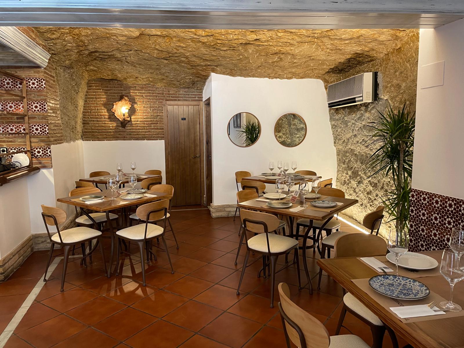 Comedor de Casa Palmero con mesas preparadas junto a la pared de roca y espejos