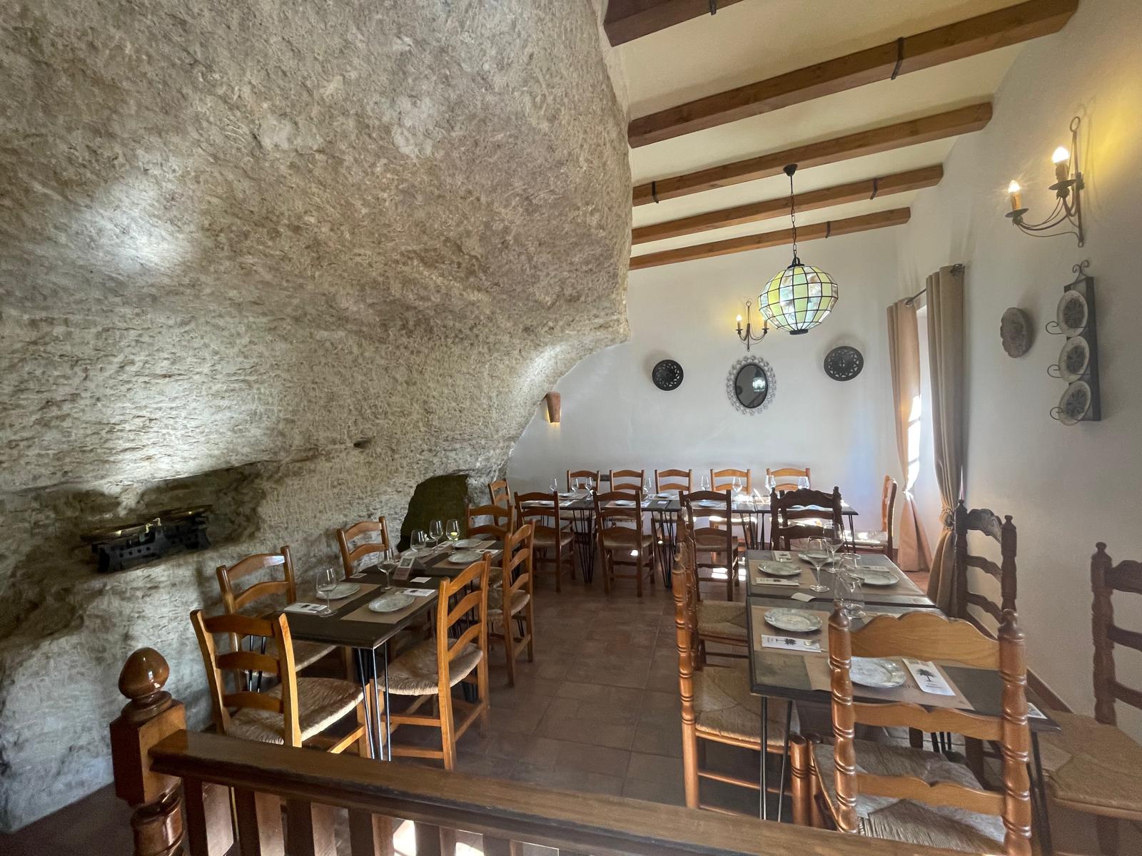 Comedor superior de Casa Palmero con vigas de madera vista y mesas junto a la roca